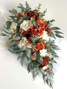 an orange and white bridal bouquet with greenery on the bottom is laying on a white surface