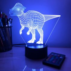 an illuminated dinosaur lamp on a table next to a remote control