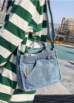 a woman carrying a blue jean purse over her shoulder and wearing a green striped shirt