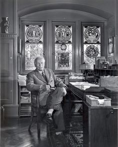 an old photo of a man sitting in front of a desk with stained glass windows