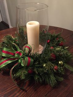 a candle is sitting on top of a christmas wreath with greenery and red ribbon