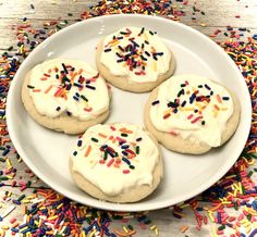 four cookies with white frosting and sprinkles on a plate