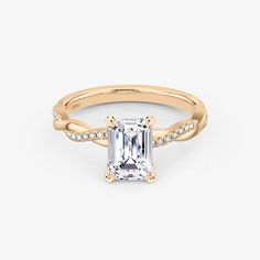 an emerald cut engagement ring with diamonds on the band and side stones in yellow gold