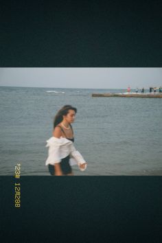 a woman walking on the beach in front of the ocean with her arms wrapped around her body