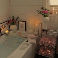 a bath tub with candles and flowers in the corner, next to a shelf filled with towels