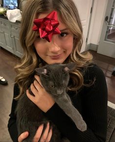 a woman holding a cat with a red bow on it's head in her hands