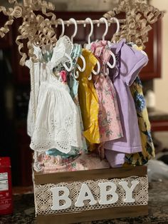 a wooden box with clothes hanging from it's sides and the word baby spelled out in white