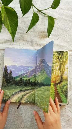 someone is holding an open book in their hands and painting it with watercolors