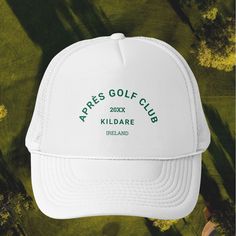 a white hat with green lettering on it and trees in the background that says apres golf club killdare ireland