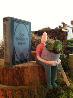 a statue sitting on top of a tree stump holding a potted plant next to a book