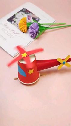 a small red toy airplane next to a card and flowers on a pink table top