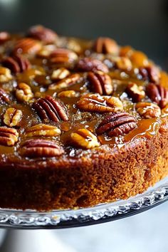 a cake with pecans and caramel on top sitting on a glass platter