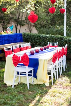 an outdoor table set up with red, white and blue paper lanterns hanging from the ceiling