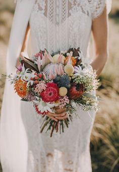 a woman holding a bouquet of flowers in her hands and wearing a white wedding dress