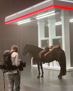 a woman standing next to a black horse in a room filled with lights and cameras