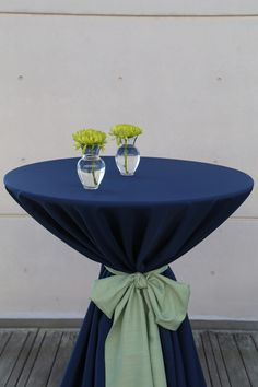 two vases with flowers sit on top of a blue table cloth draped over it