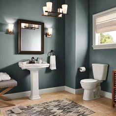 a white toilet sitting next to a sink in a bathroom under a mirror and lights