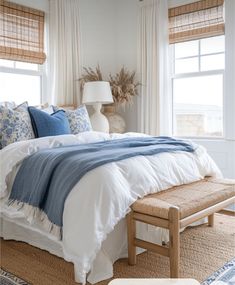 a bed with blue and white comforter in a bedroom next to two large windows