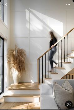 a woman is walking up the stairs in a house with white walls and wood floors