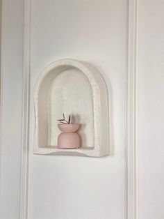 a white shelf with a pink vase on it and an arch in the wall behind it