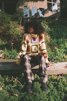 a woman sitting on top of a wooden bench in front of a house and grass