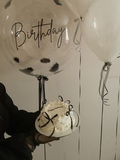 a person holding a cake and balloons with writing on them