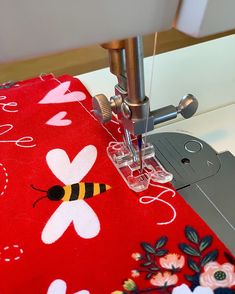 the sewing machine is working on the red flowered tablecloth with a yellow and black bee