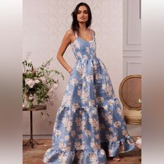 a woman in a blue and white dress standing next to a vase with flowers on it