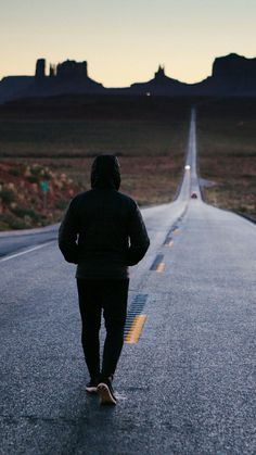 a man walking down the middle of an empty road at dusk with his back to the camera