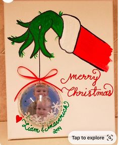 a christmas ornament hanging from the side of a white card with a green and red hand holding a baby's head