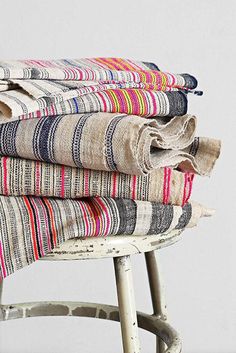 a stack of folded towels sitting on top of a wooden stool next to a white wall