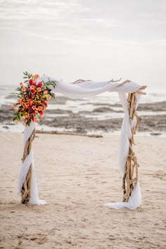 an outdoor wedding setup on the beach with white draping and flowers in vases