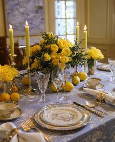 the table is set with yellow roses and silverware, candles, and china plates