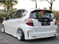 the rear end of a white honda fit car parked in a parking lot next to trees