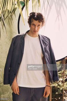 a man standing in front of a palm tree wearing a jacket and t - shirt