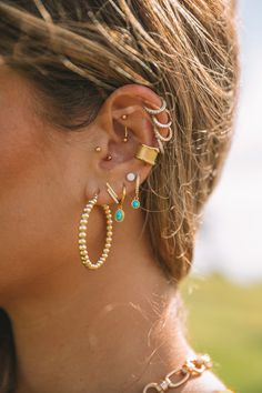 a close up of a woman's ear wearing gold and turquoise earrings with pearls