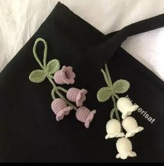 two crocheted flowers are on top of a black tote bag with green leaves