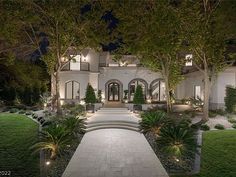 a large white house with lots of trees and bushes in front of it at night