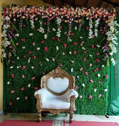 a white chair sitting in front of a green wall with flowers on it's side