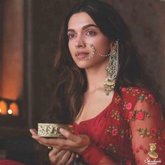 a woman in a red dress holding a cup and nose ring with pearls on it