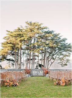 an outdoor ceremony set up with wooden chairs and flowers on the grass, surrounded by tall trees