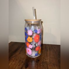 a glass with flowers painted on it and a straw sticking out of the top is sitting on a wooden table