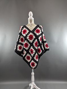 a black and white crocheted sweater on a mannequin head with red flowers