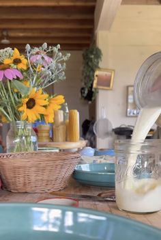 a person pouring milk into a jar on top of a table with flowers in the background