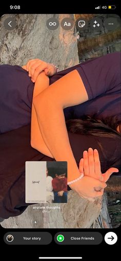 a woman laying on top of a bed next to a stone wall with her hands in the air