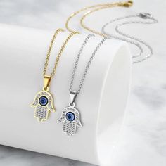 Featuring a delicate Hamsa Hand pendant adorned with sparkling cubic zirconia stones and a captivating evil eye, this necklace is a symbol of good luck, health, and happiness.  What's Included: 1 x Necklace or Necklace Set of 2 Pendant Size: 1cmx1.5cm Key Features: *Symbolic Design: Combines the protective power of the Hamsa Hand and Evil Eye *Sparkling Cubic Zirconia: Adds a touch of glamour and elegance *Gold/Silver Finish: Choose the perfect metal to match your style *Delicate Chain: Creates Silver Spiritual Necklace With Cubic Zirconia, Spiritual Silver Cubic Zirconia Necklace, Spiritual Silver Necklace With Cubic Zirconia, Silver Cubic Zirconia Charm Necklaces, Tarnish Resistant, Silver Tarnish Resistant Charm Necklaces With Cubic Zirconia, Silver Metal Jewelry With Evil Eye, Silver Metal Evil Eye Jewelry, Silver Cubic Zirconia Charm Necklaces For Jewelry Making, Silver Pendant Necklace With Diamond Eyes