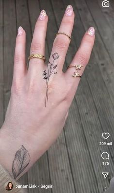 a woman's hand with tattoos on it and flowers tattooed on the middle finger