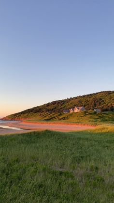 a grassy field next to the ocean with houses on top of a hill in the distance