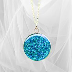 This beautiful circular glitter pendant necklace is crafted with precision using the finest quality resin and glitter, set in a 1-inch round stainless-steel setting, and finished with either a 20" silver-plated chain or a 20" black waxed necklace cord. Its vibrant green hue and sparkly finish will brighten up any outfit and make you stand out from the crowd. Ideal for special occasions. Party Necklace With Large Round Pendant, Glitter Round Jewelry As Gift, Round Glitter Jewelry As Gift, Round Glitter Jewelry For Gifts, Silver Glitter Necklace For Gift, Blue Handmade Crystal Round Pendant Necklace, Blue Crystal Round Pendant Necklace For Gift, Blue Spiritual Round Pendant Necklace, Green Resin Round Pendant Necklace