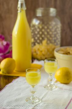 two glasses filled with yellow liquid sitting on a table next to some lemons and a bottle